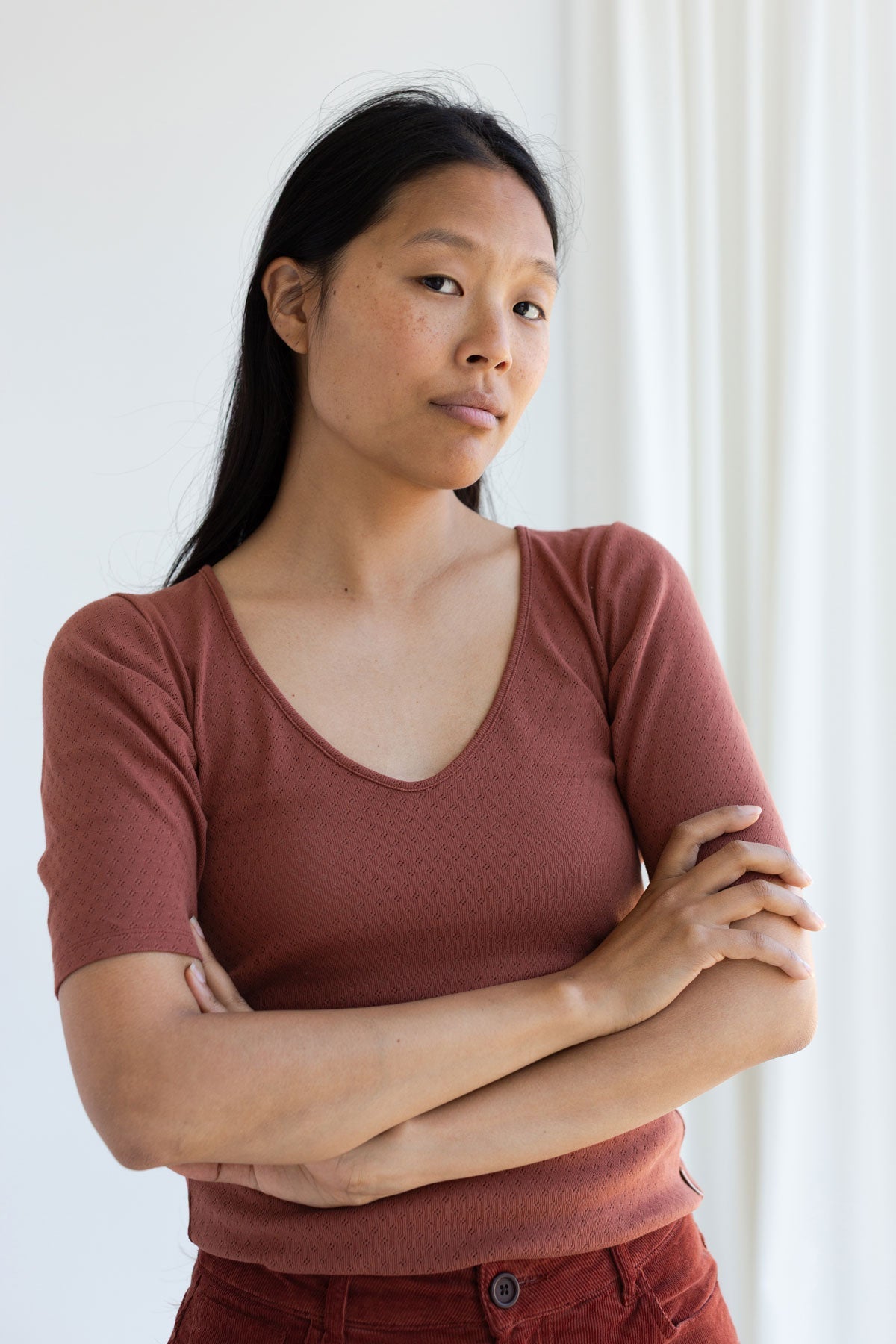 Woman wearing a brown slim-fit pointelle V-neck top with arms crossed.