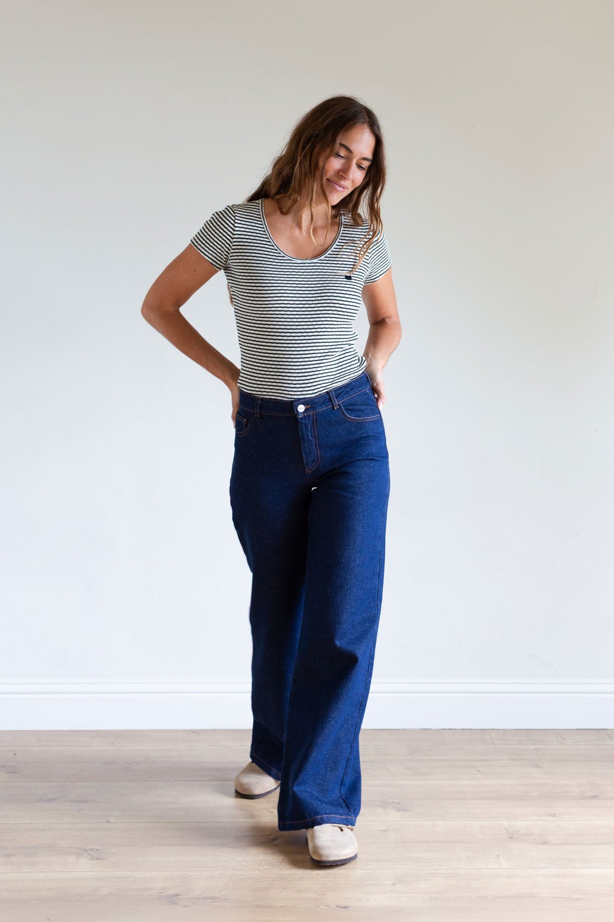 Full body view of a woman in a dark green striped ribbed top and wide-leg jeans.