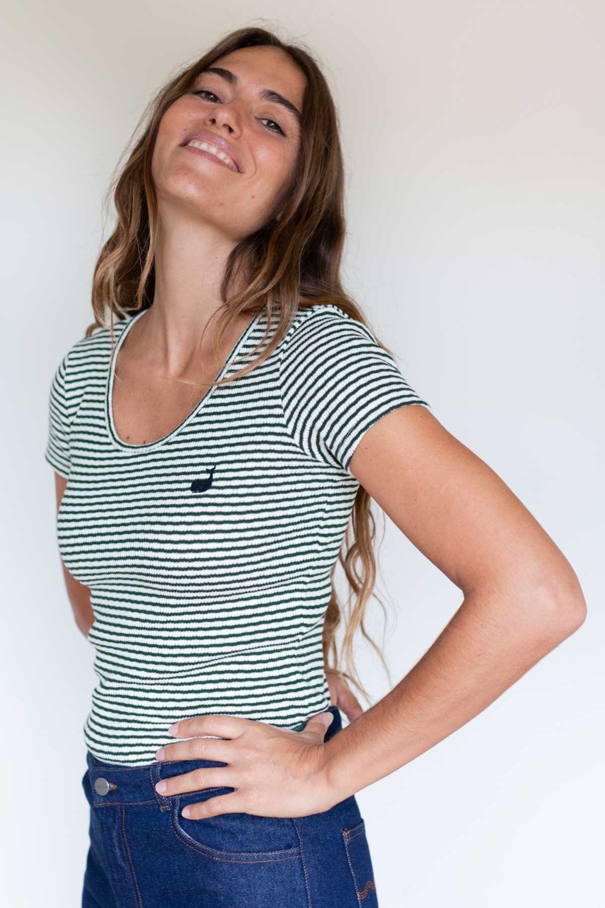 Woman smiling in a dark green striped slim-fit ribbed shirt.