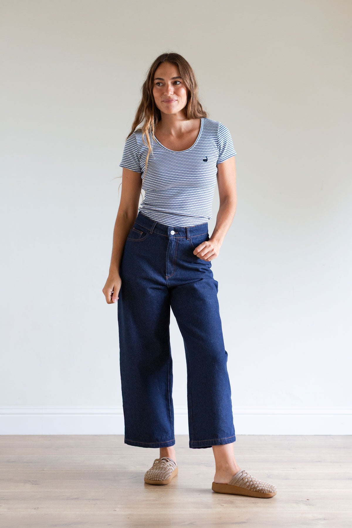 Full body shot of a woman in a blue striped ribbed top and dark blue jeans.