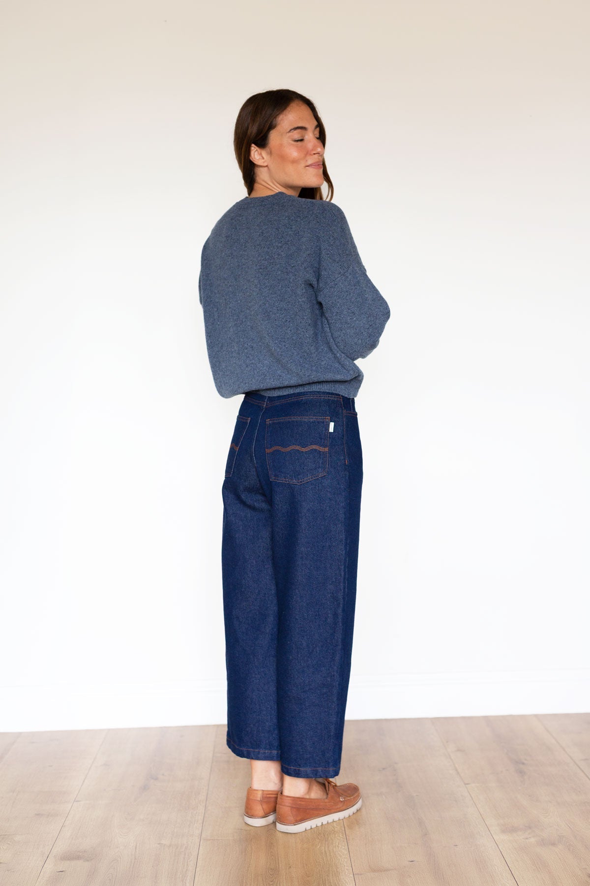 Back view of a woman wearing a slightly cropped, relaxed-fit blue knit sweater and dark jeans.