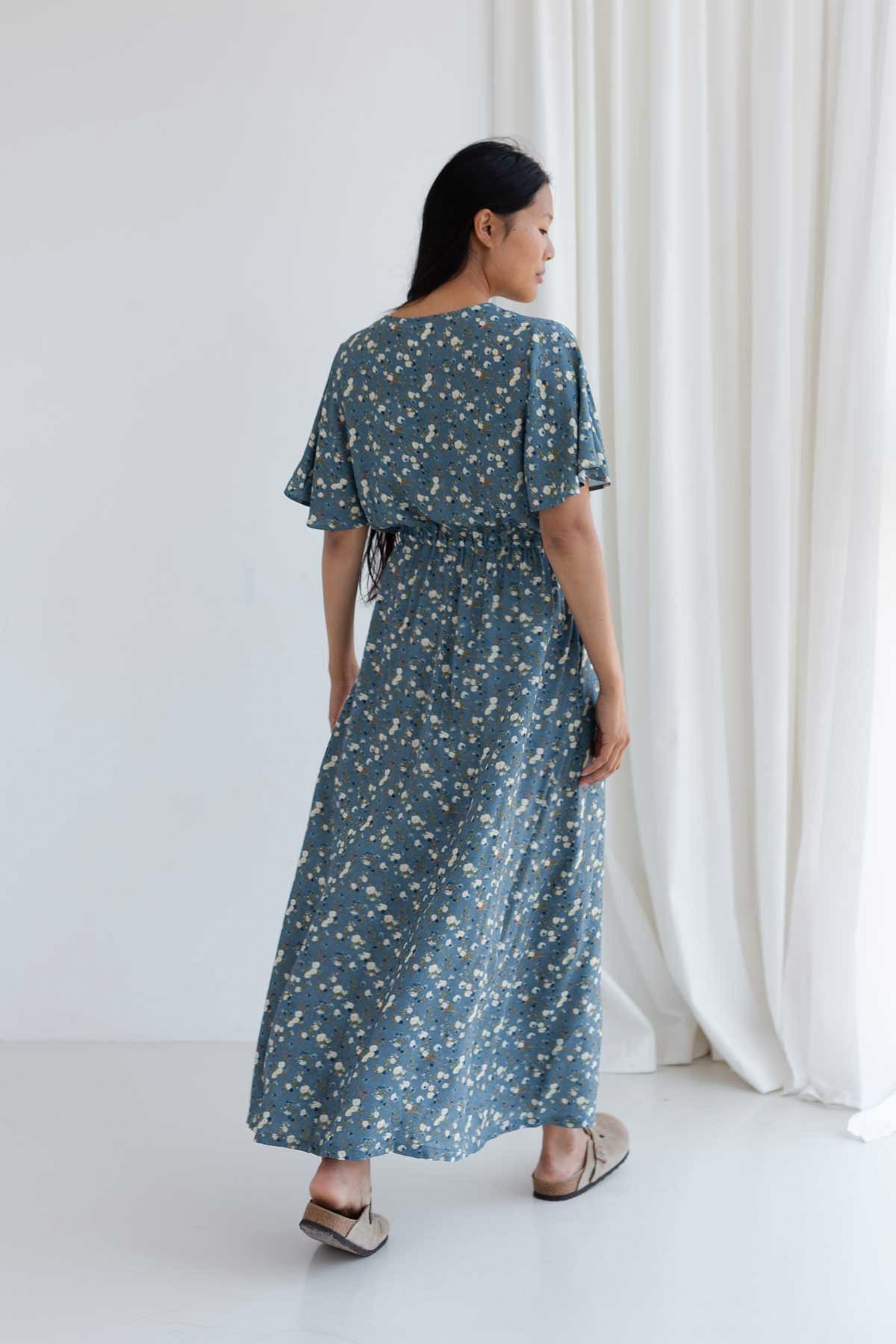 Full body back view of a woman wearing a blue floral viscose midi dress.
