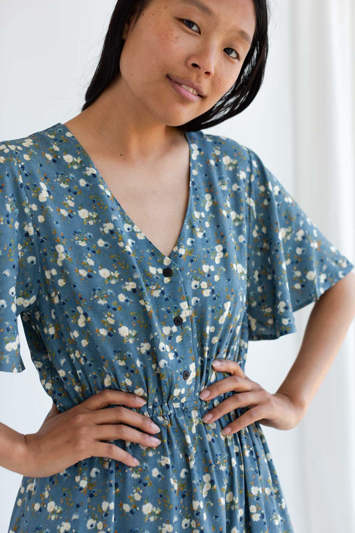 Woman with hands on her hips wearing a blue floral V-neck midi dress with buttons and an elasticated waist.