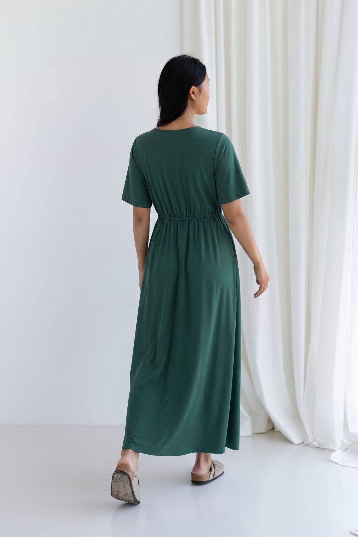 Full body back view of a woman wearing a garden green midi dress with an elasticated waist.