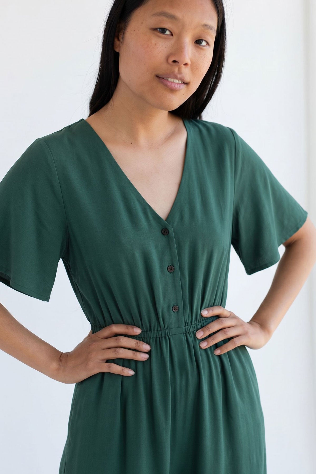 Front view of a woman wearing a garden green V-neck midi dress with buttons and an elasticated waist.