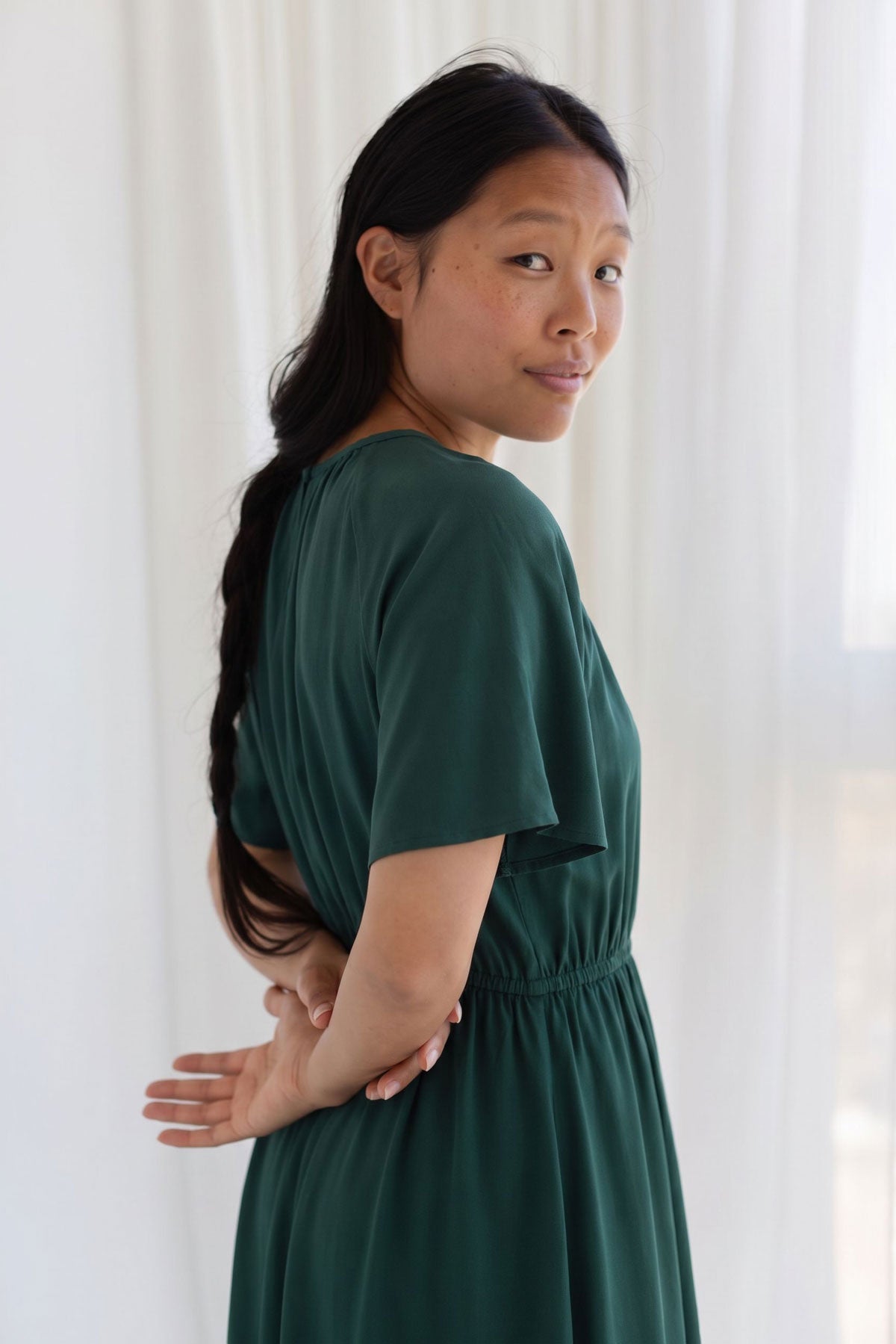 Side profile view of a woman in a garden green midi dress with her hands behind her back.