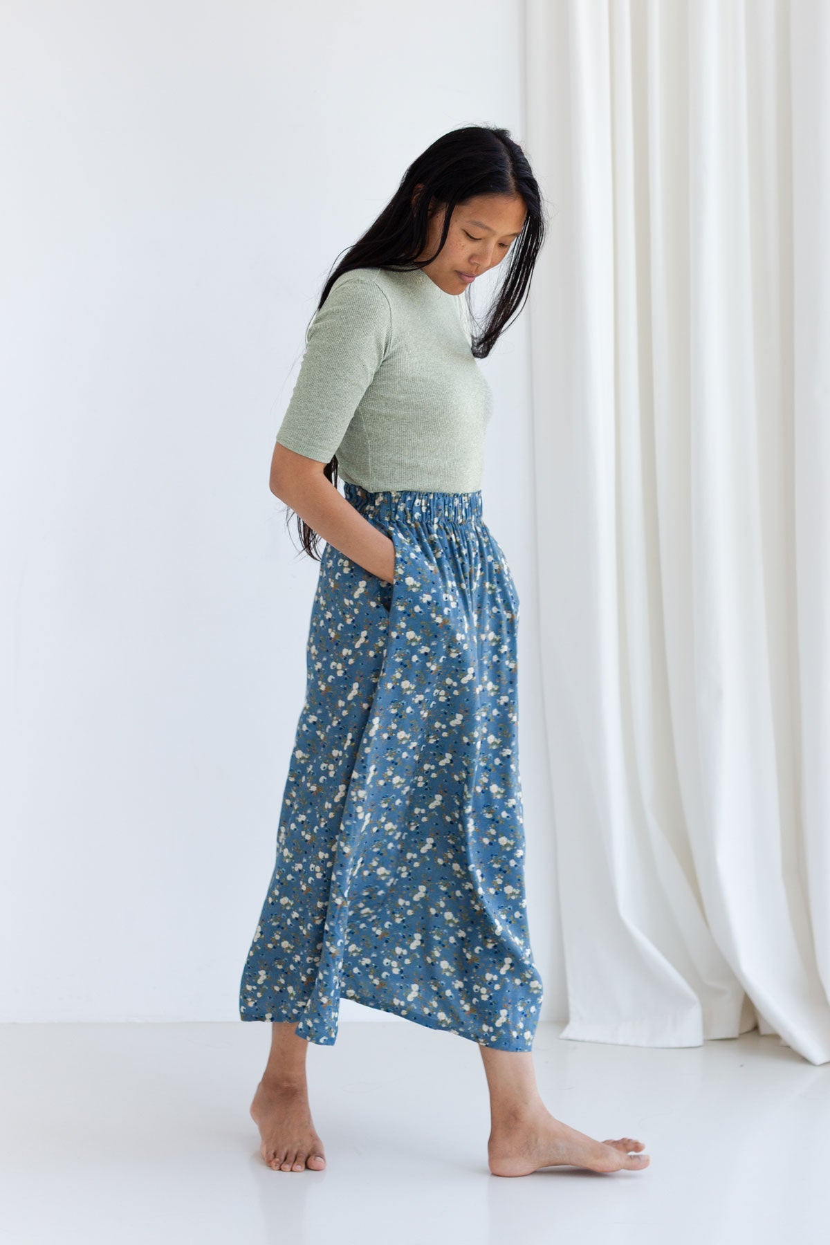 Full length side profile of a woman in a desert sage green ribbed top and a blue floral midi skirt.