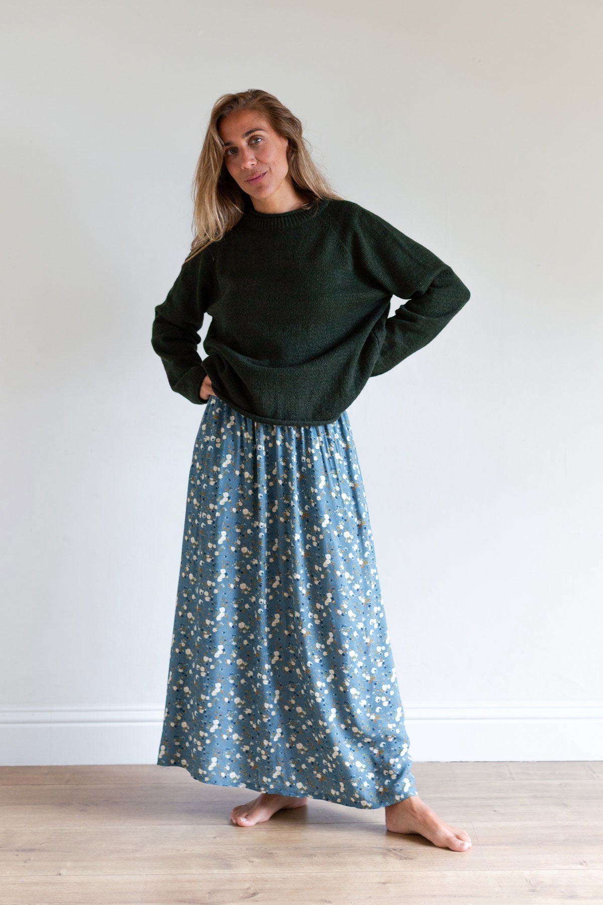 Woman posing in a blue floral maxi skirt and a dark green knit sweater.