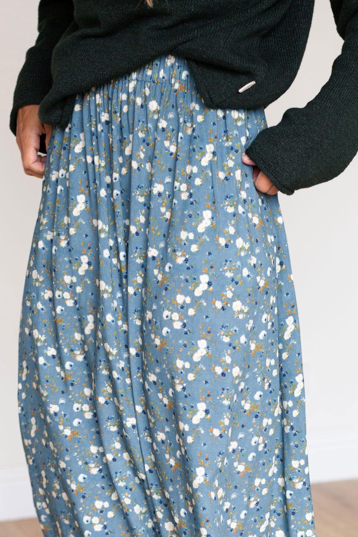 Close-up detail of a blue floral A-line maxi skirt with hands in its side pockets.