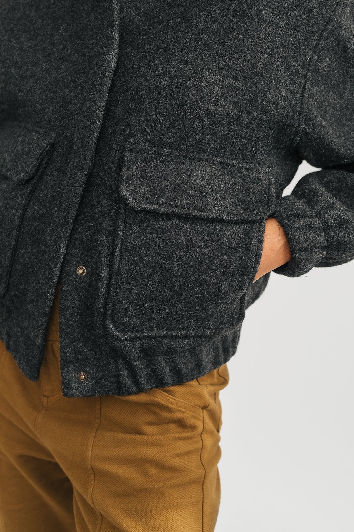 model with hands in wool grey jacket front pockets, showcasing rubber cuffs.
