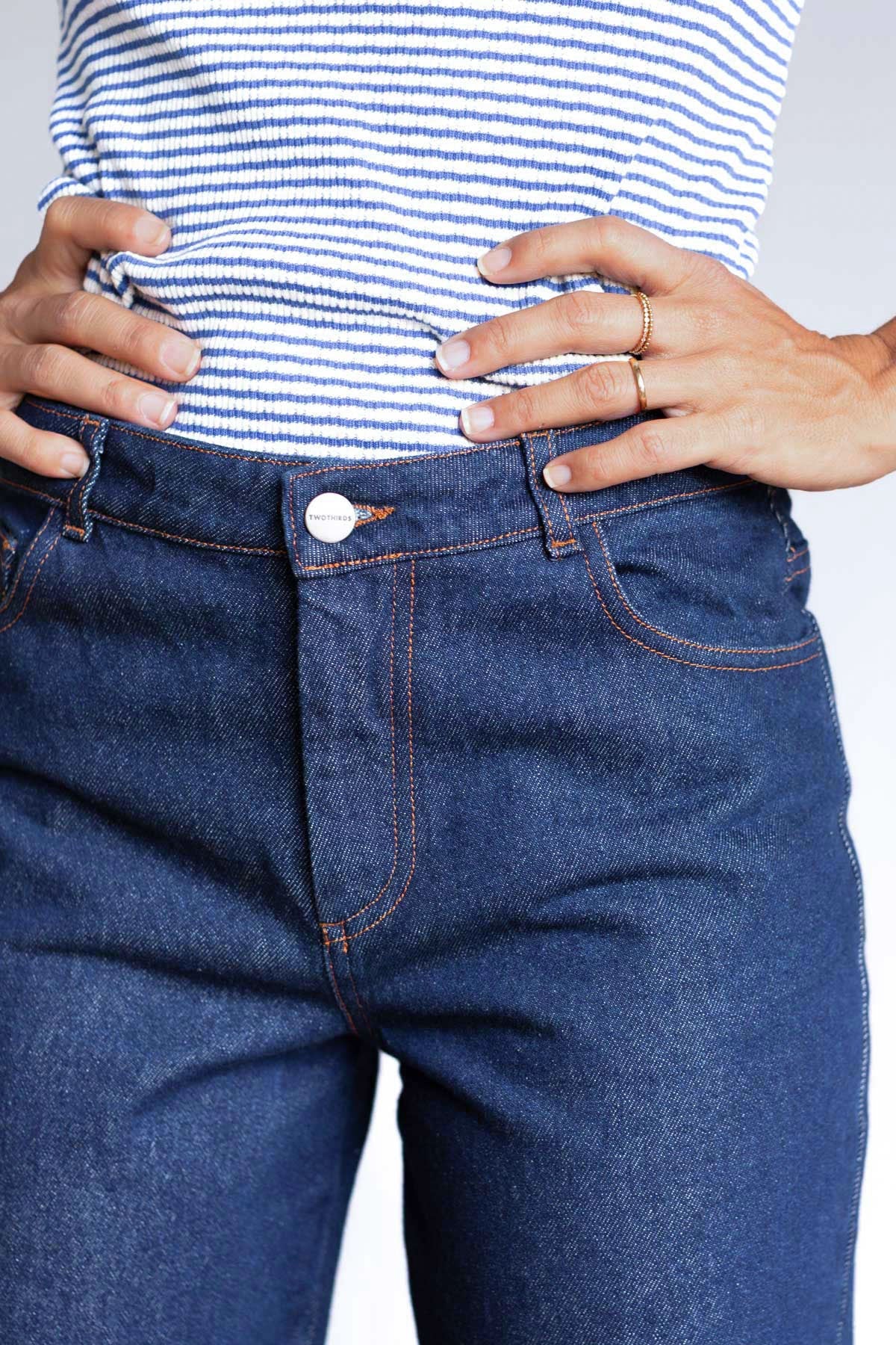 Close-up front view of the waist and embossed button closure on blue denim pants.