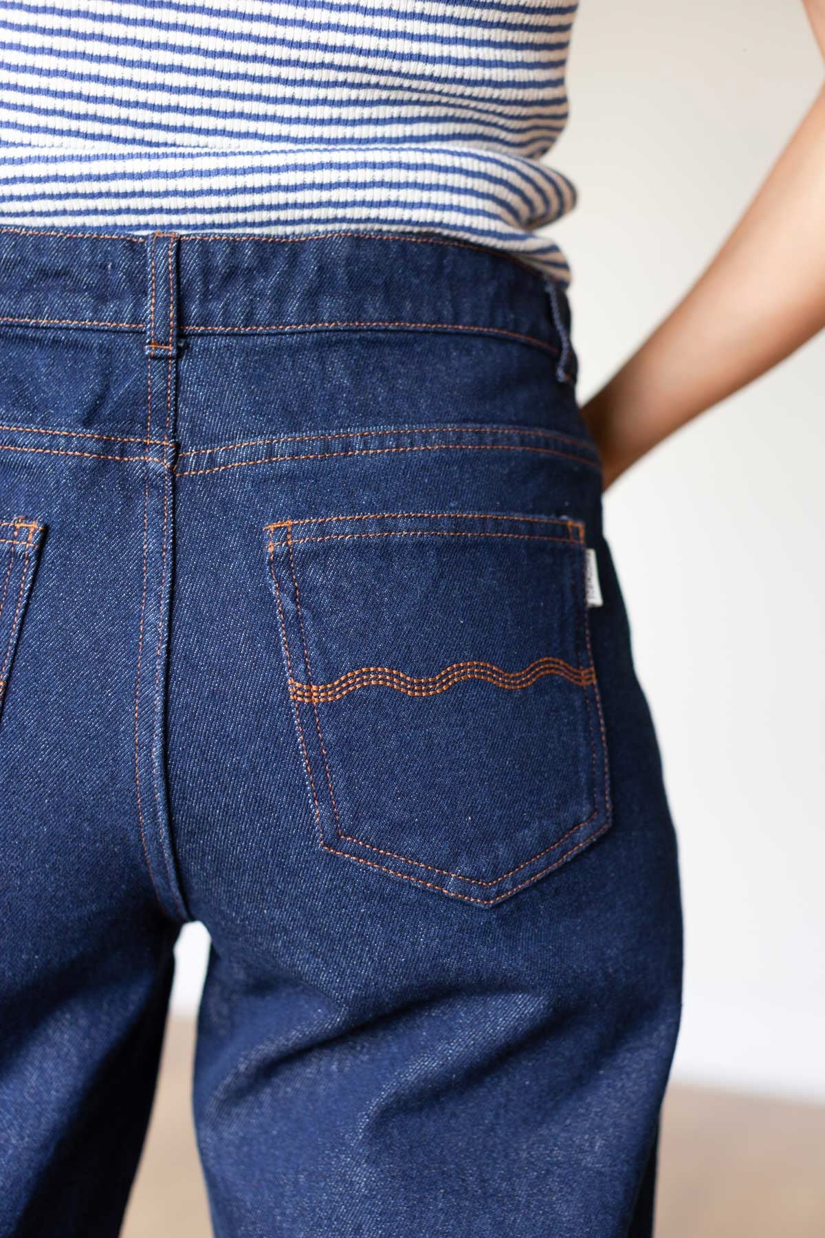Back view detail showing the stitched pockets on dark blue denim pants.