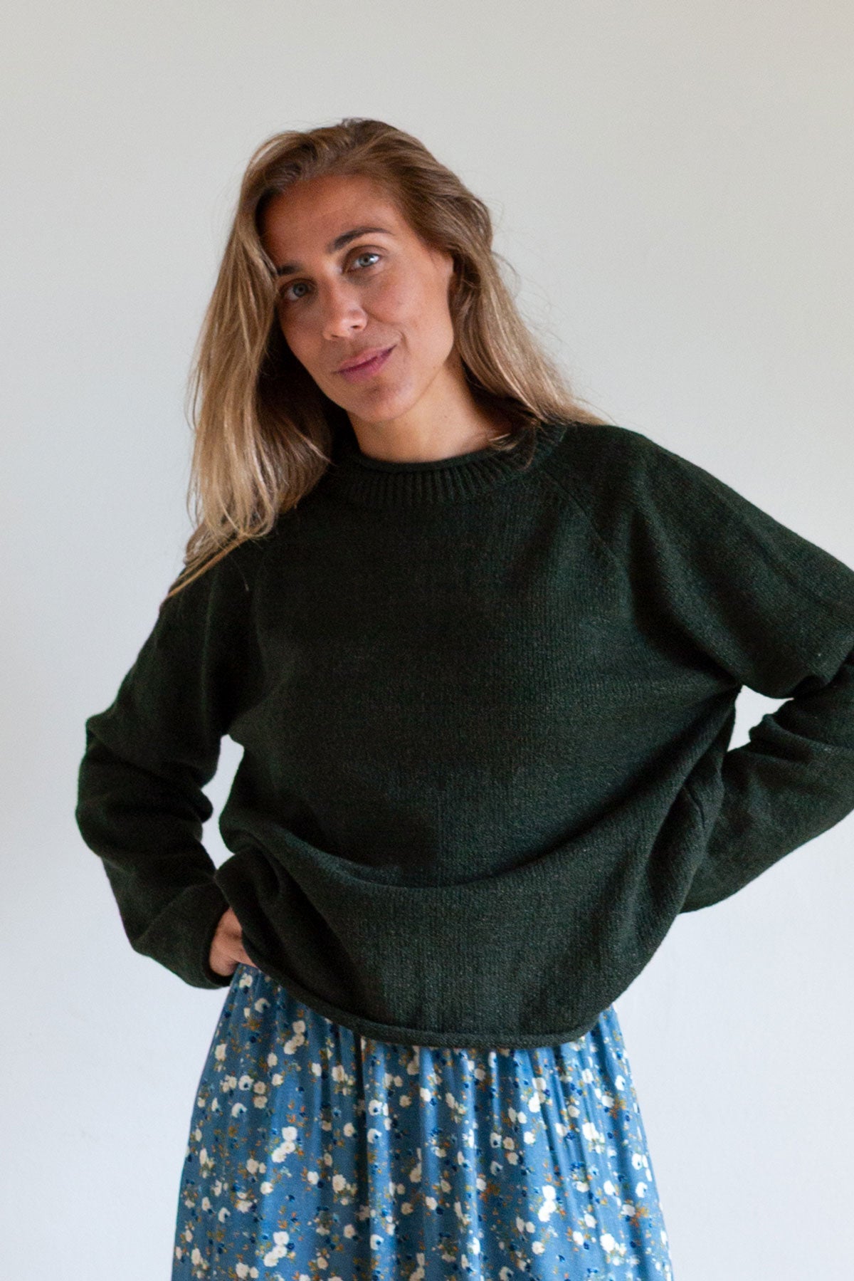Woman posing with hands on hips in a dark green raglan sweater.