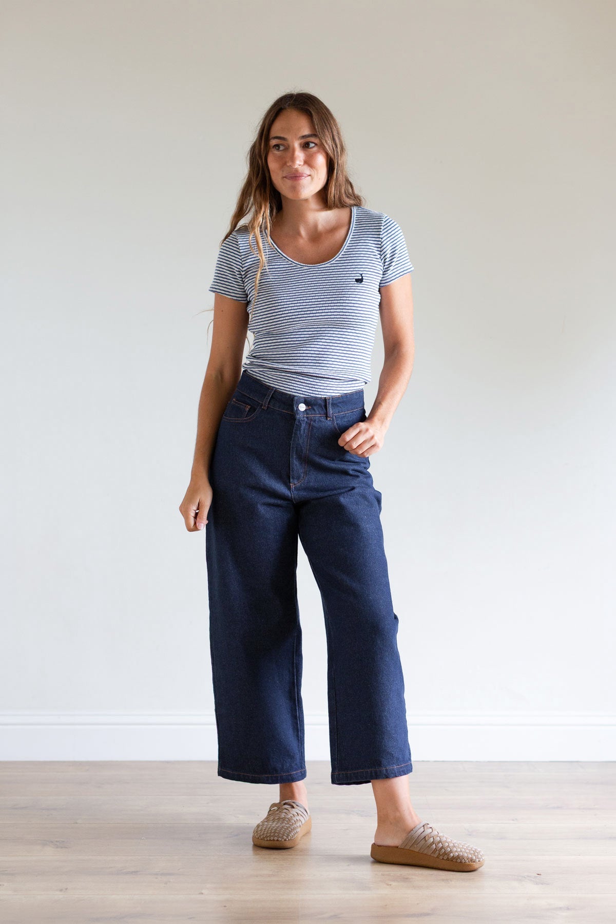 Full body front view of a woman wearing ankle-length wide-leg blue denim pants.