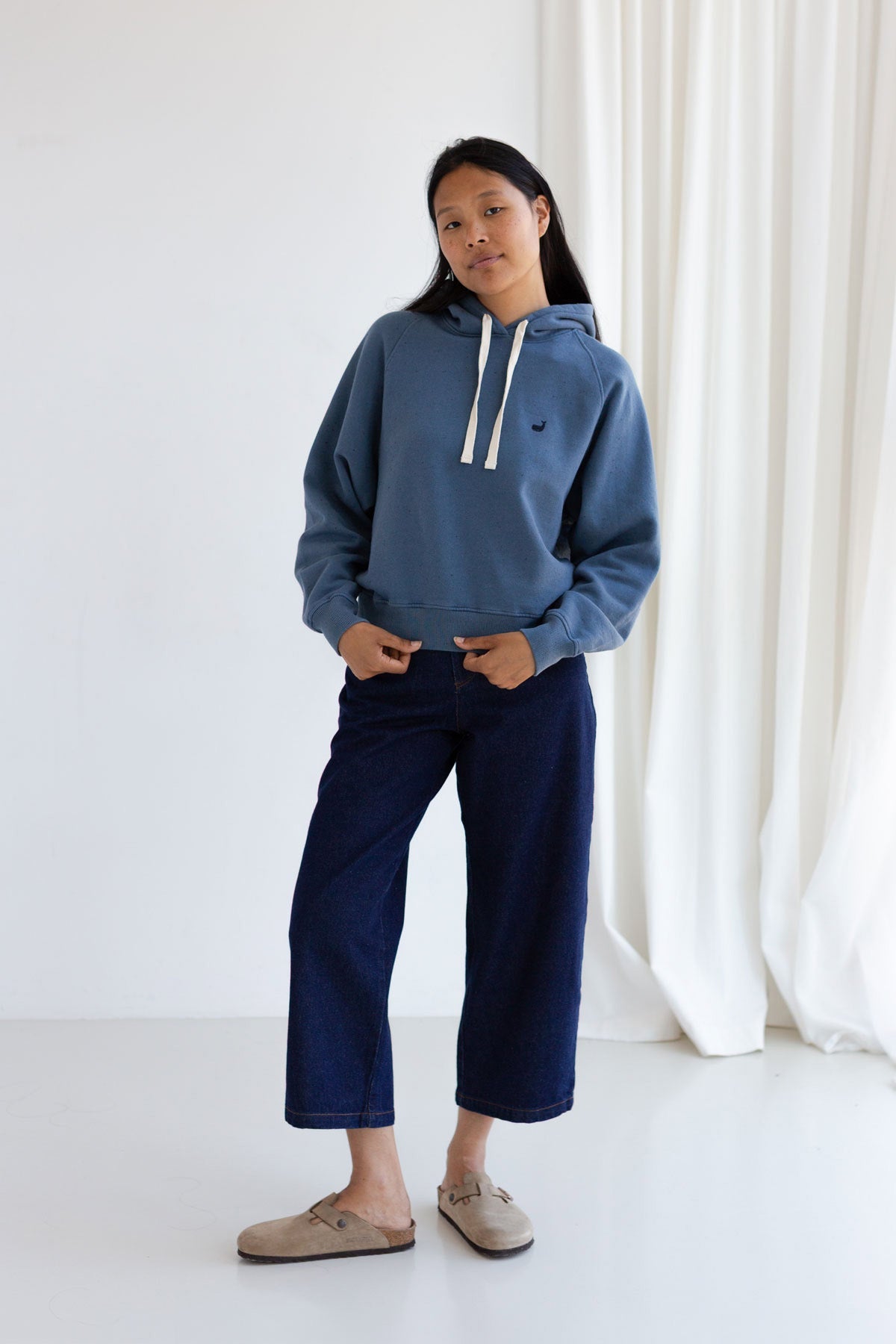 Full body front view of a woman wearing a dusty blue hoodie and wide-leg jeans.