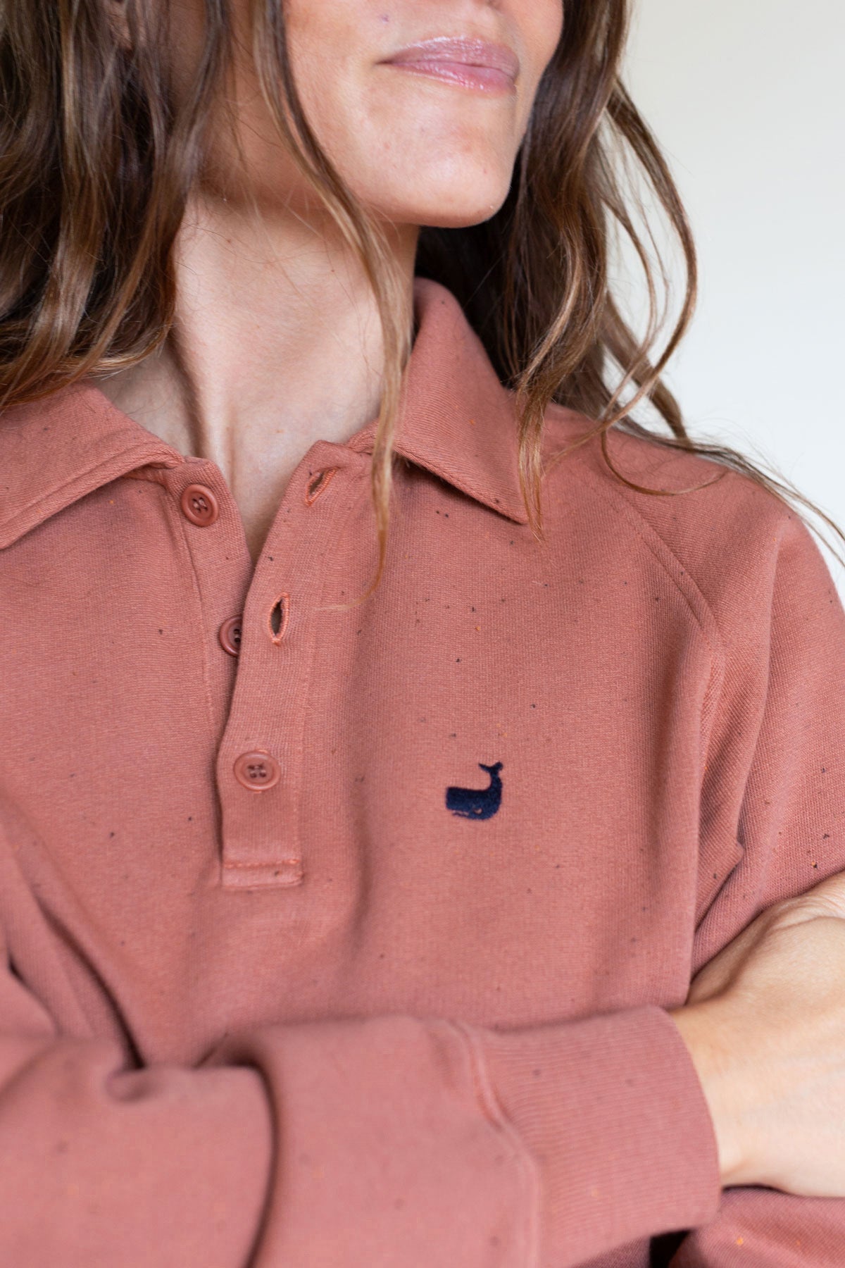 Close-up front view of the button collar and embroidered whale on a rose polo sweatshirt.