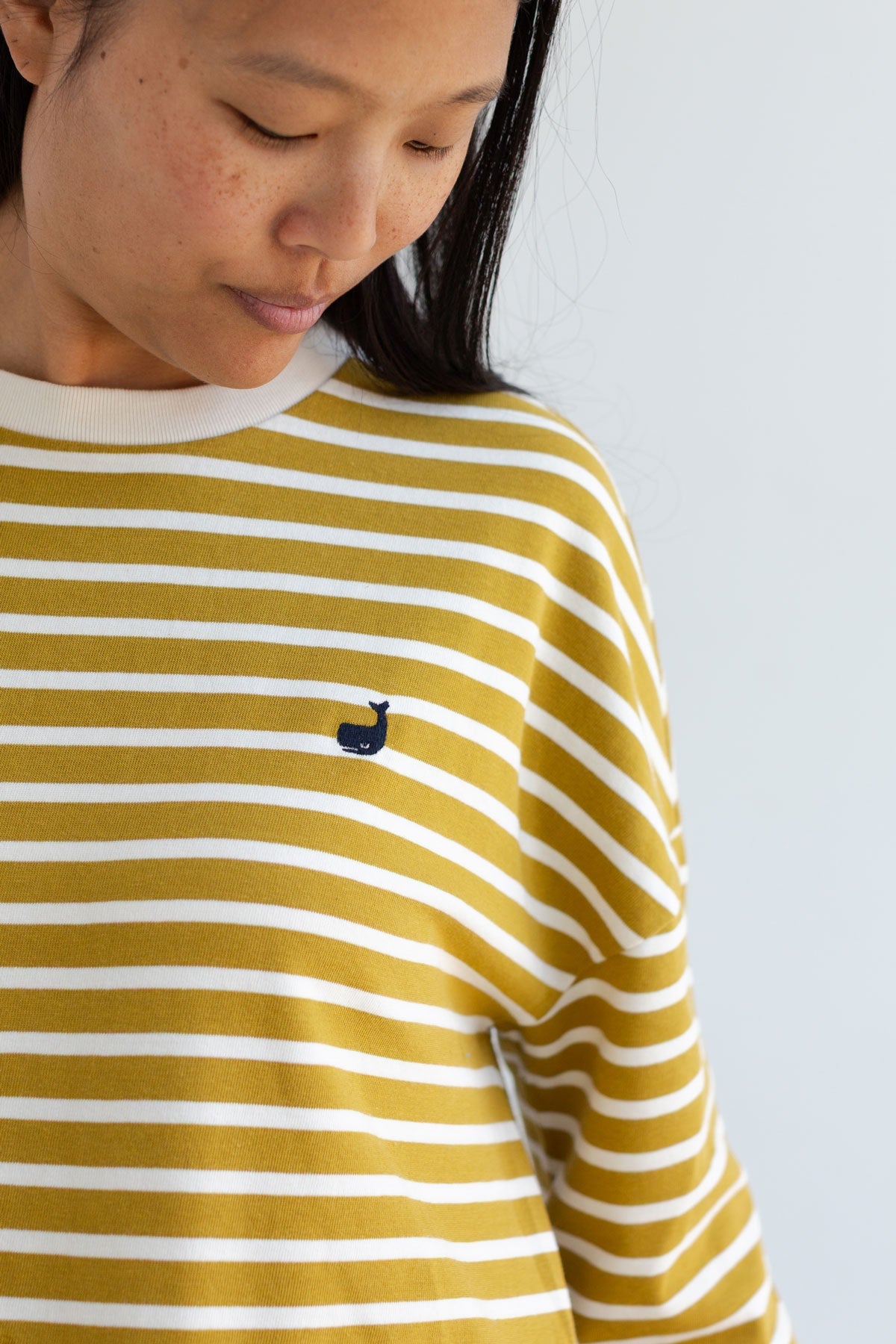 Close-up of a mustard yellow striped top with a small embroidered whale.