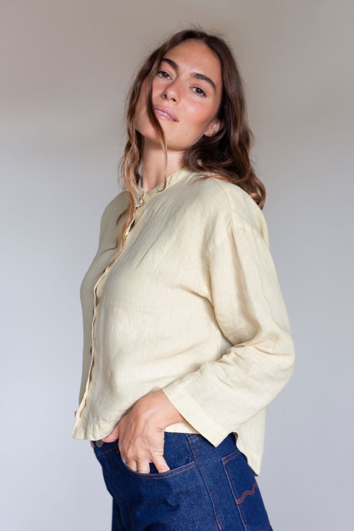 Side profile view of a woman wearing a gardenia yellow linen shirt with 3/4 sleeves.