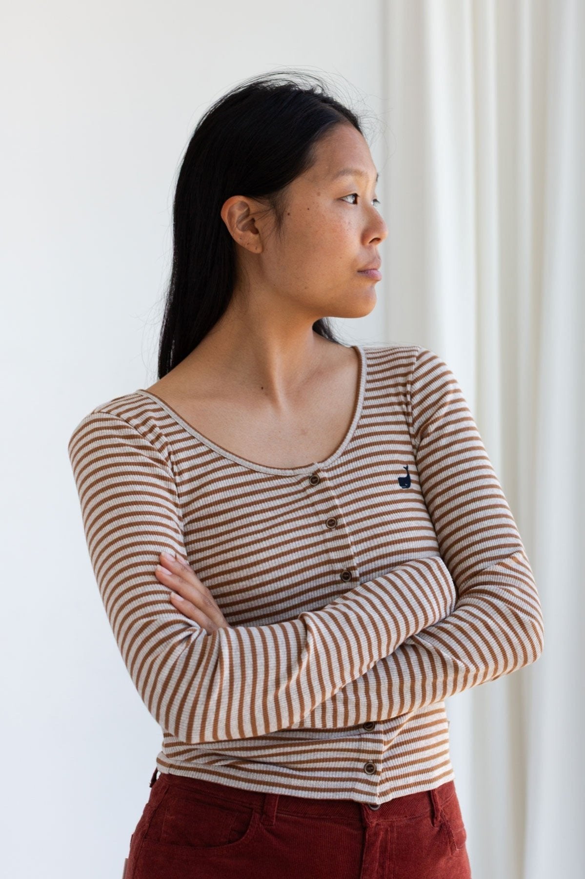 Woman with arms crossed wearing a caramel striped ribbed long sleeve top with buttons.