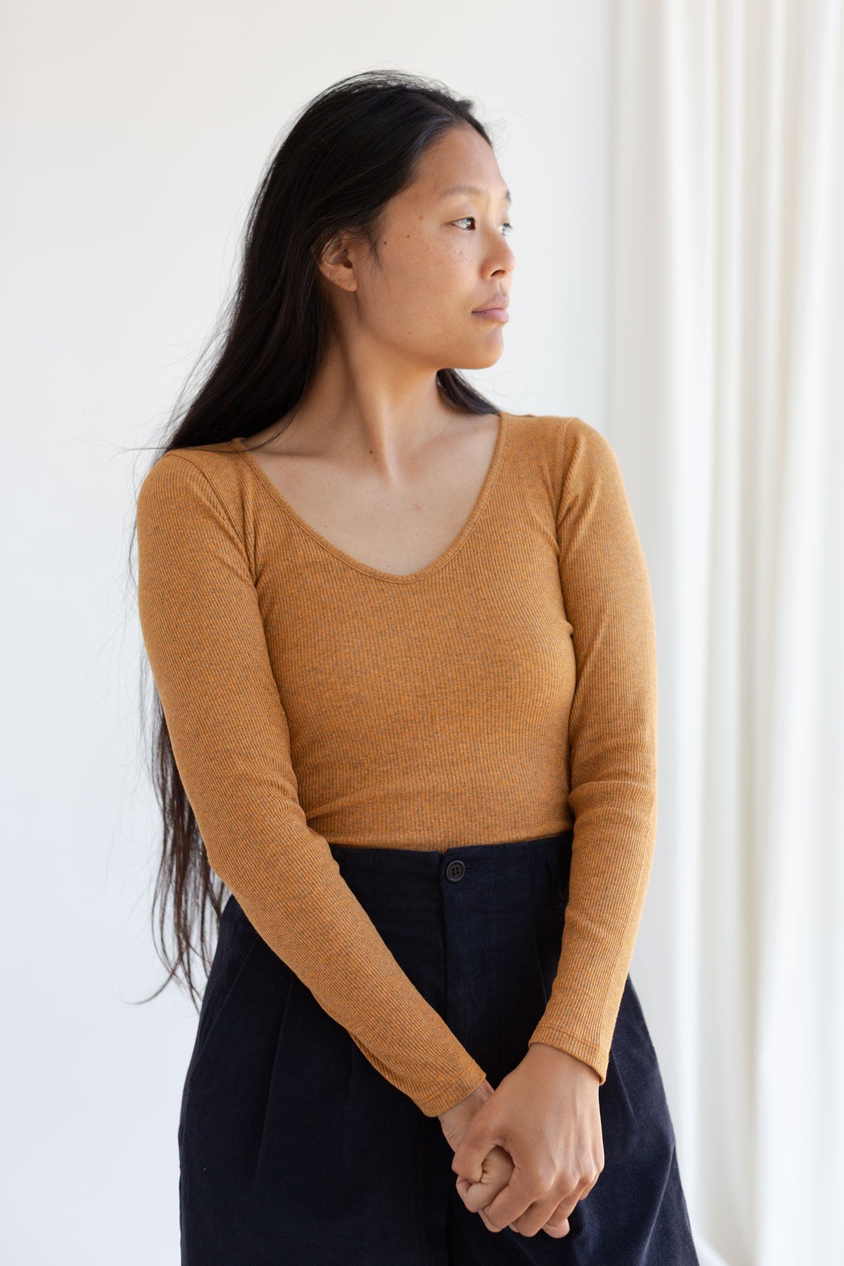 Woman wearing a nugget-yellow long sleeve scoop-neck top tucked into dark blue corduroy trousers.