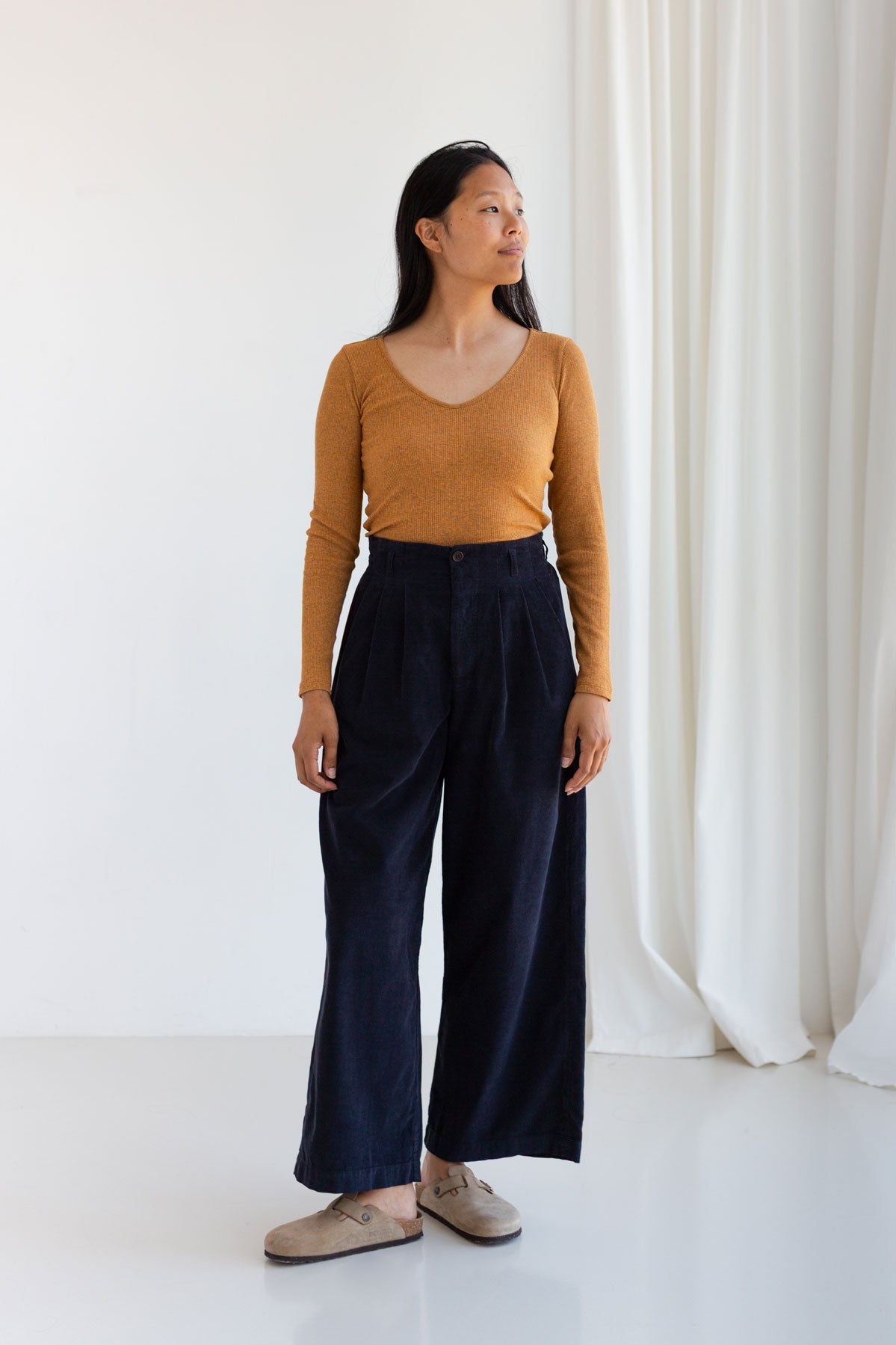 Woman standing in a nugget-yellow ribbed top and dark blue corduroy pants.