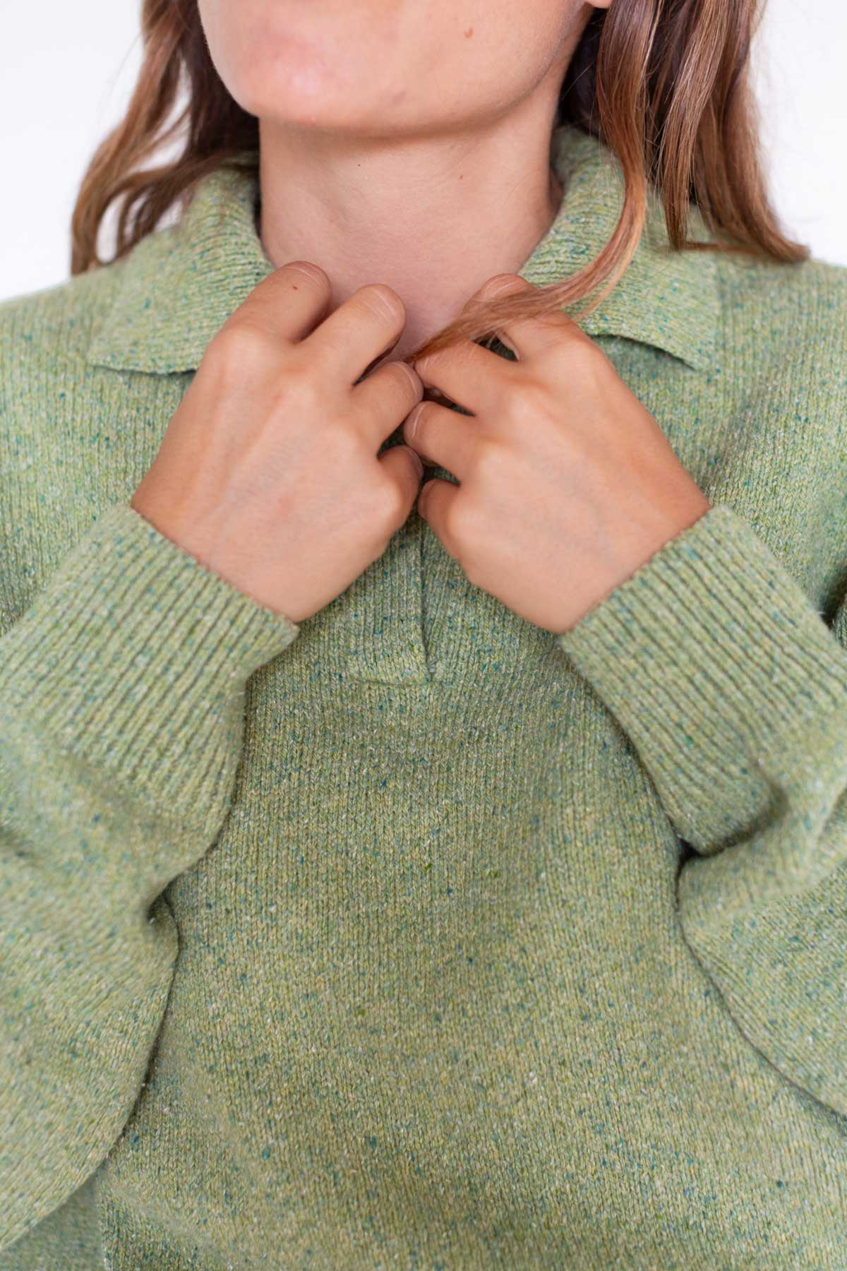 Close-up of a woman adjusting the open collar of a matcha green knit sweater.