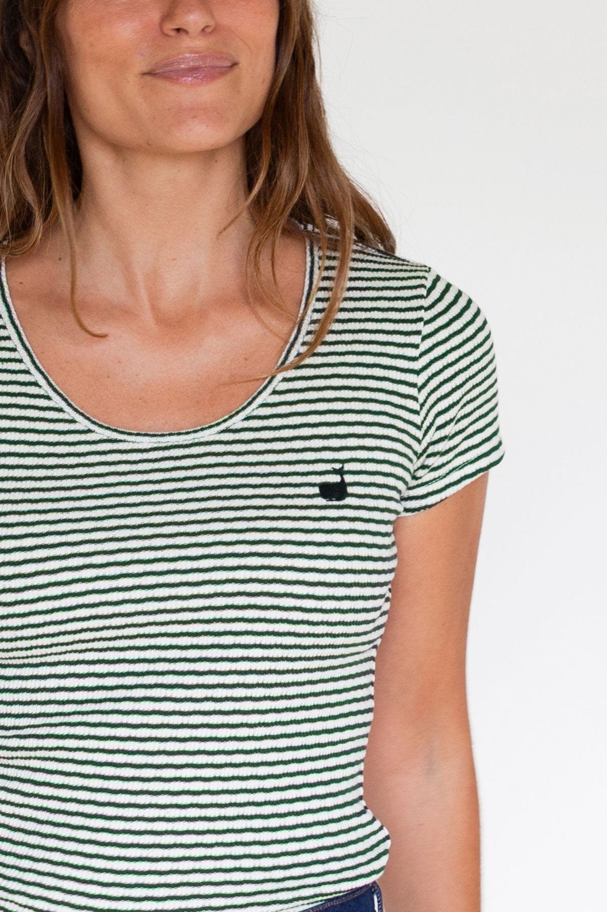 Close-up view of a dark green striped scoop neck top with an embroidered whale.