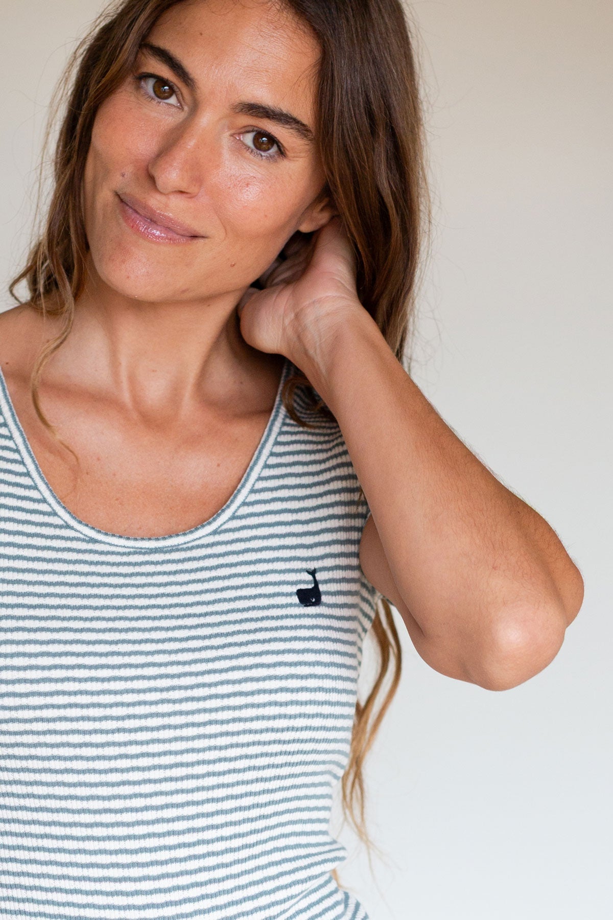 Close-up front view of a woman wearing a sage green striped top with a small whale logo.