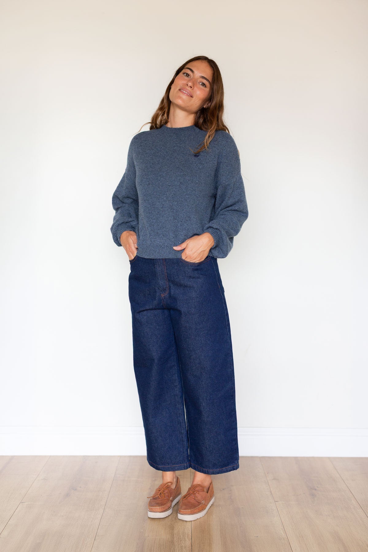 Full body shot of a woman in a blue relaxed-fit knit sweater and dark wide-leg jeans.