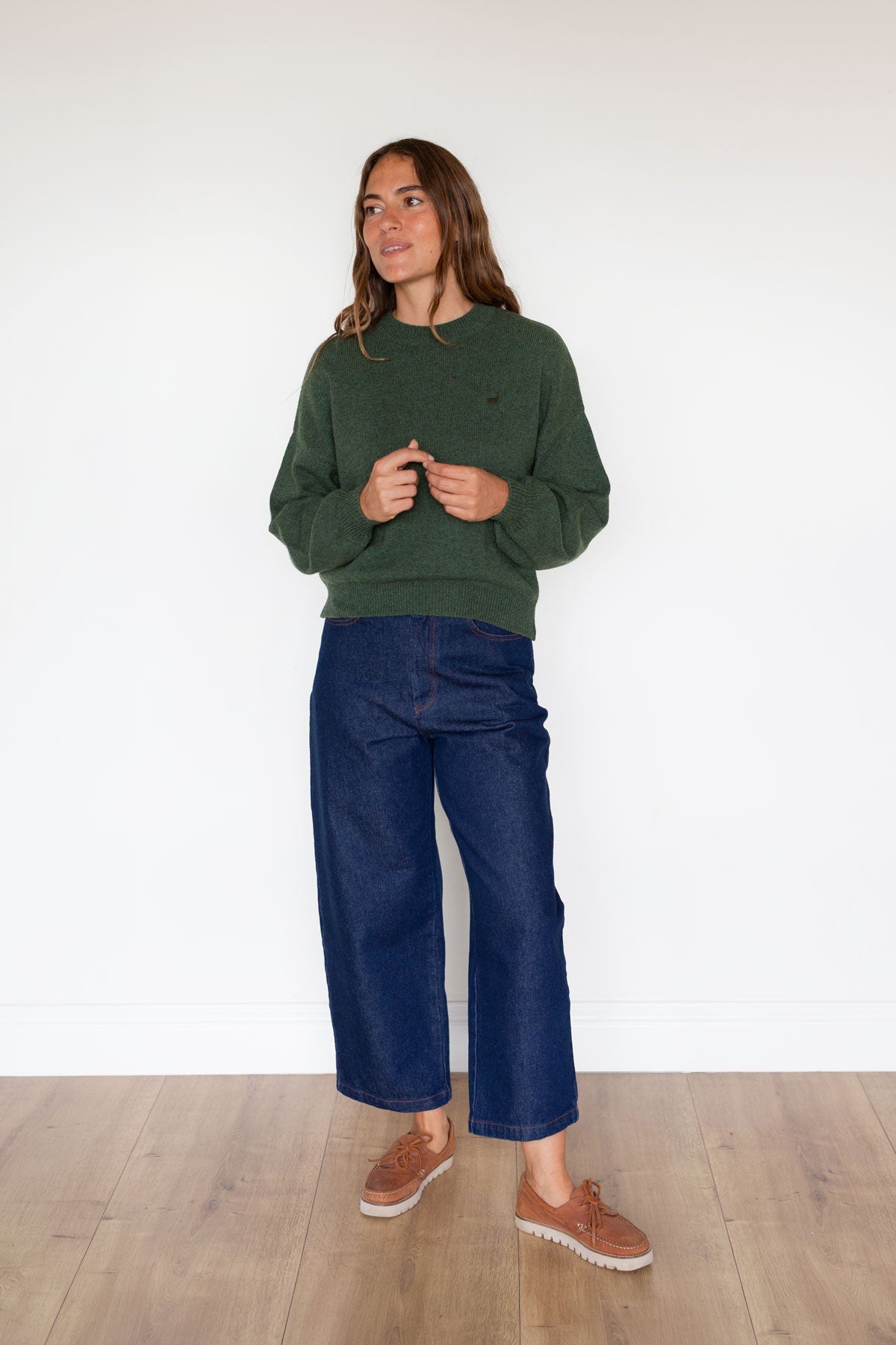 Full body shot of a woman wearing a green relaxed-fit knit sweater and dark blue jeans.