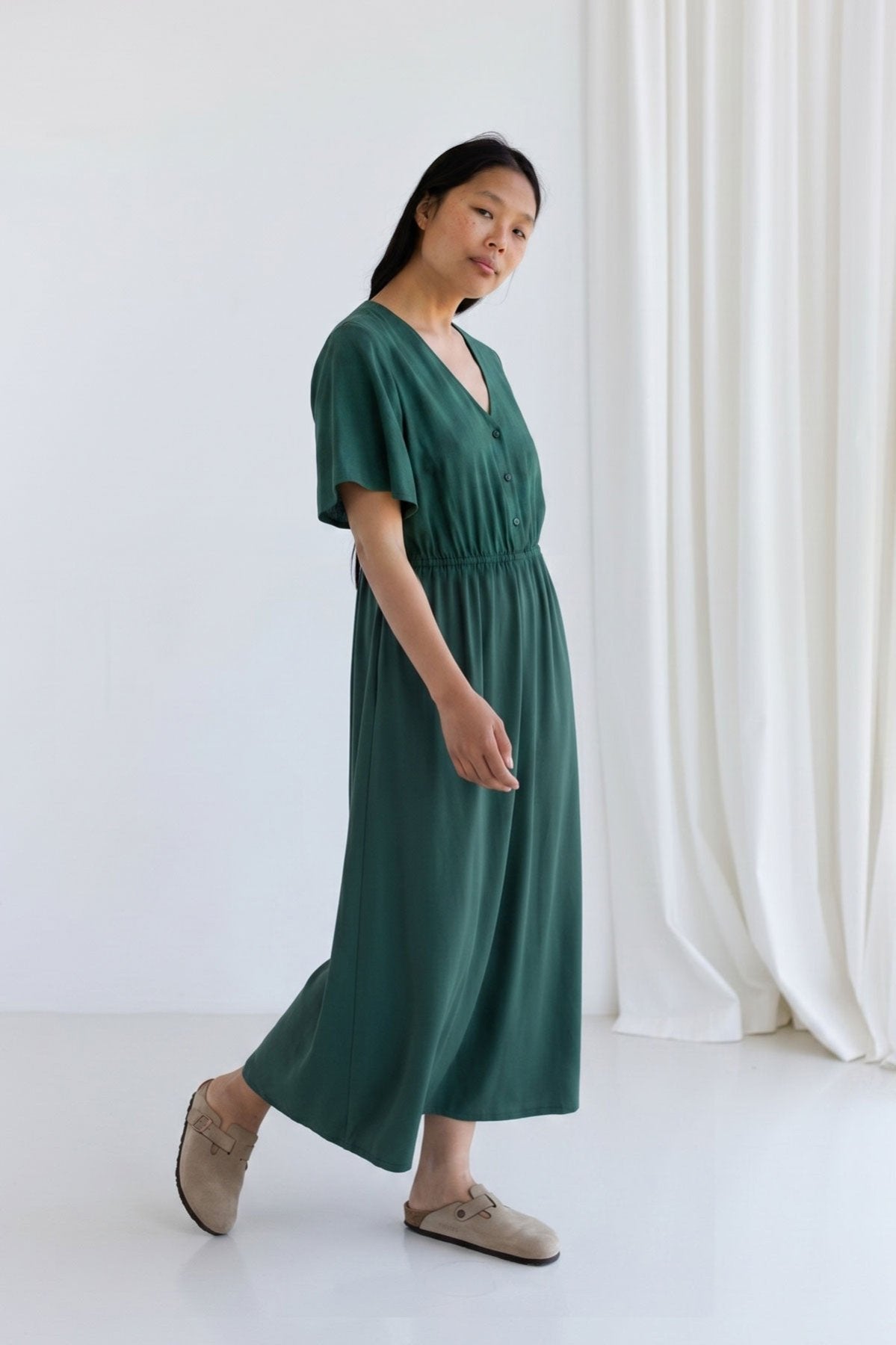 Full body side view of a woman walking in a garden green viscose midi dress.