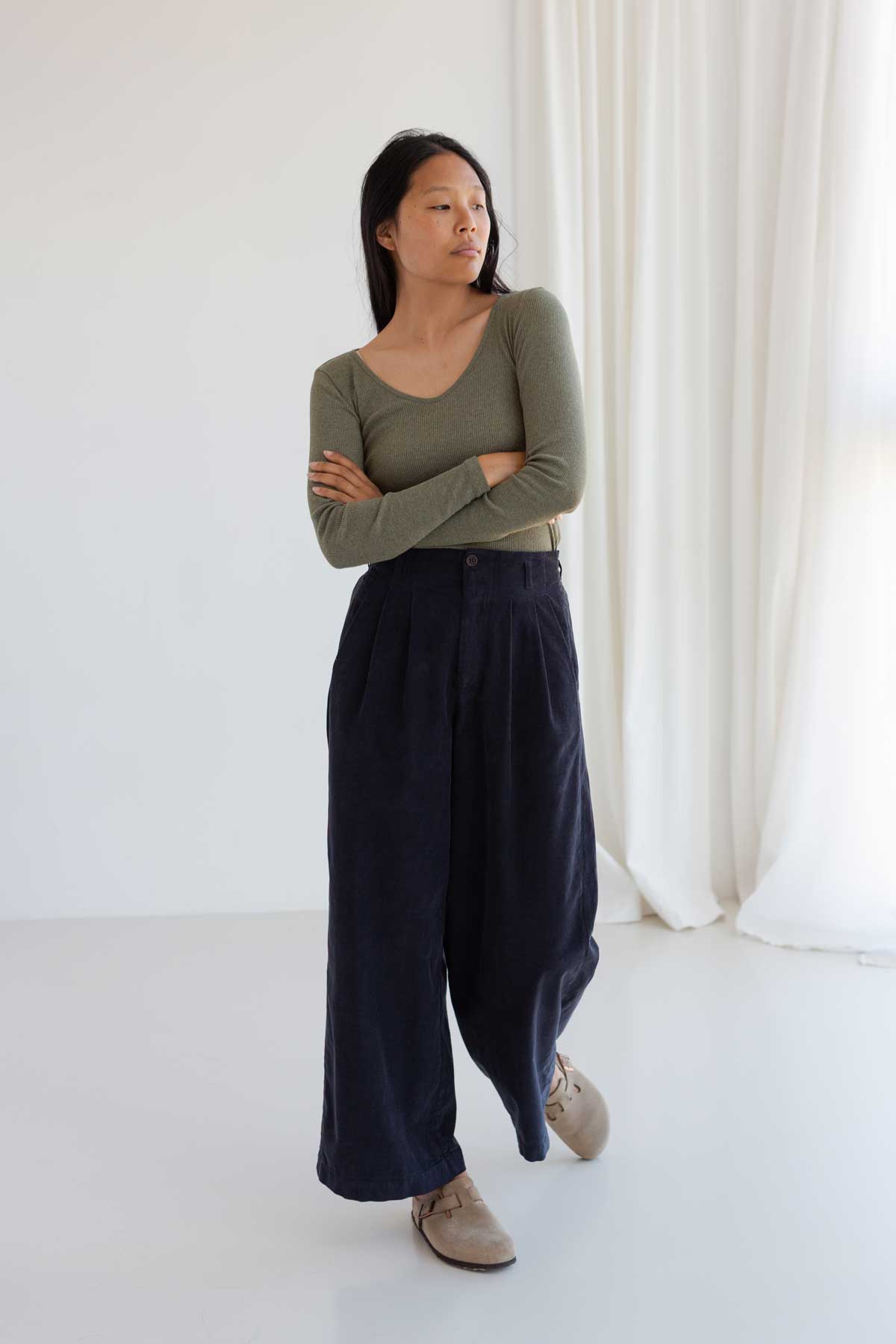 Full body shot of a woman with arms crossed in high-waist wide-leg midnight blue micro corduroy pants.