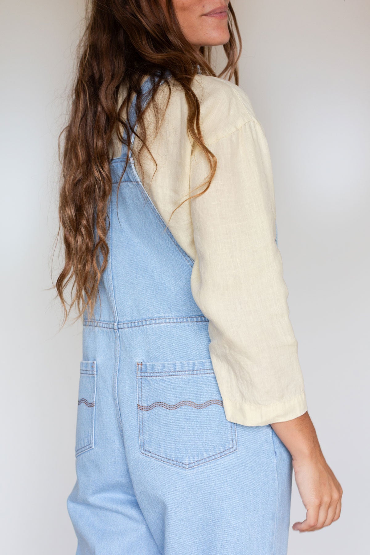 Side back view showing the pocket embroidery on light blue denim overalls.