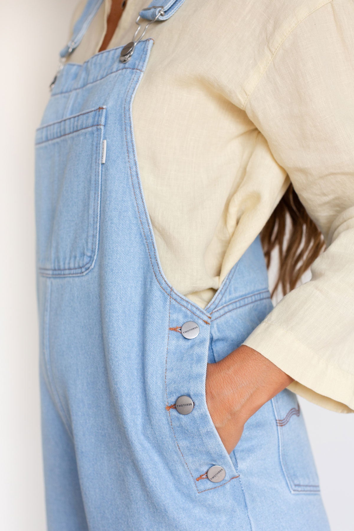 Close-up of side metal buttons and pocket detail on light blue denim overalls.