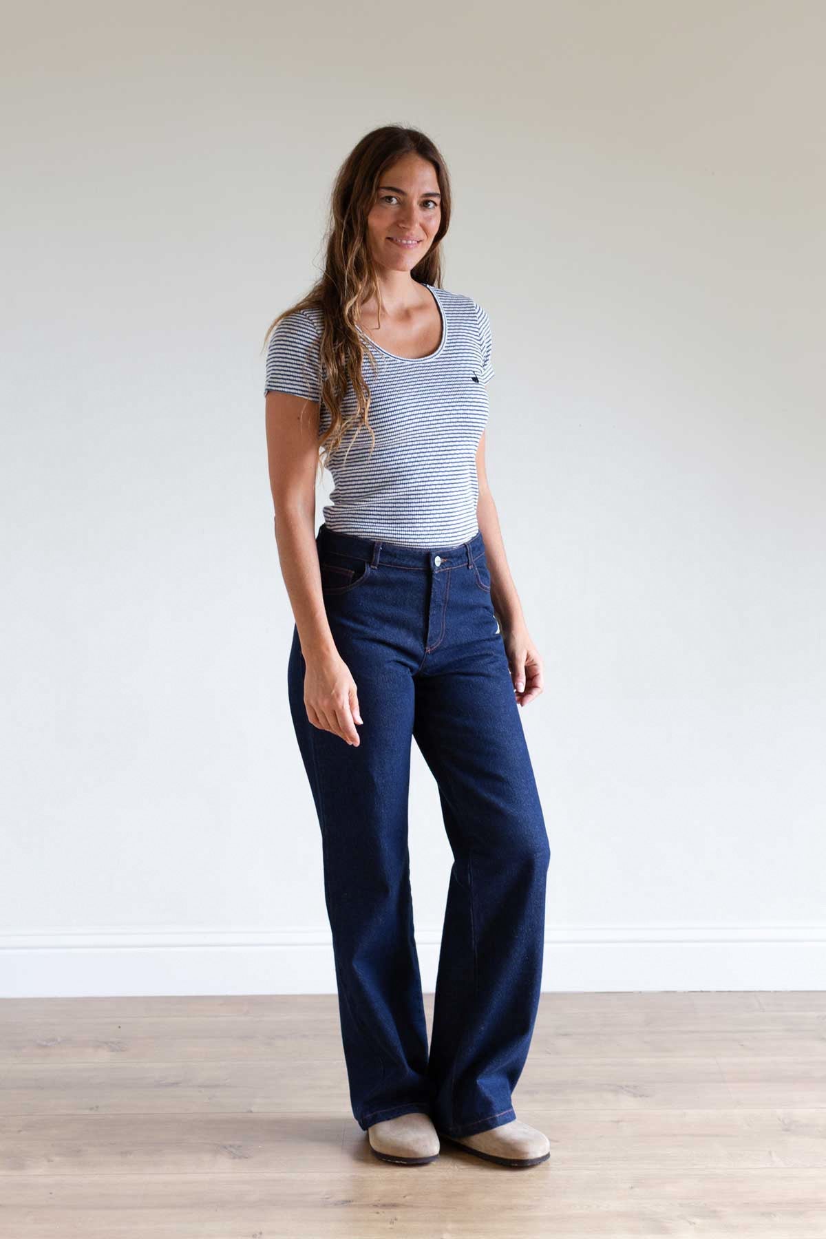 Full body shot of a woman standing wearing dark blue denim pants and a striped t-shirt.