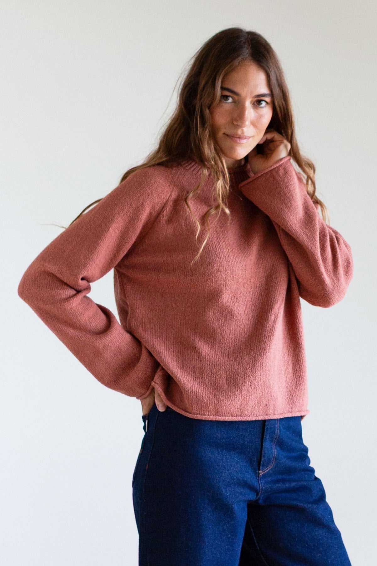Woman wearing a rose-colored raglan knit sweater and blue jeans.
