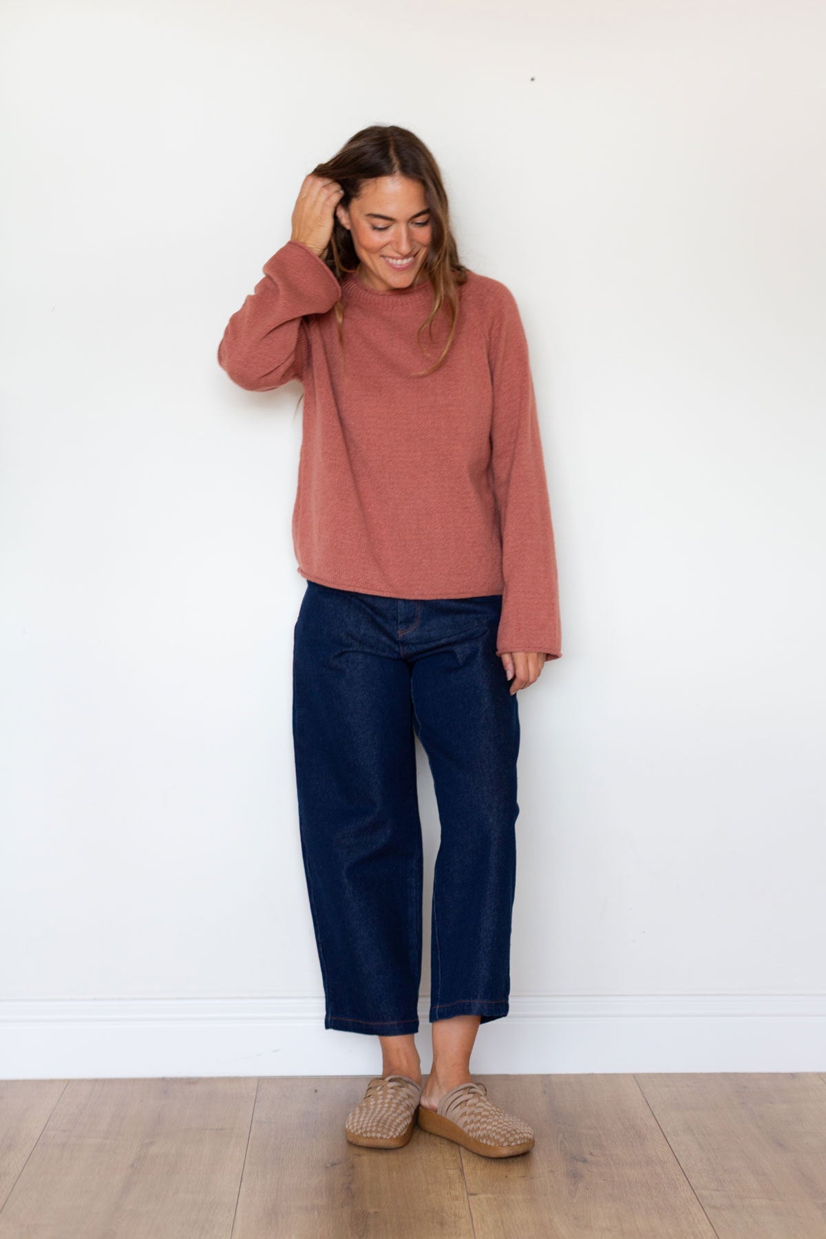 Full body shot of a woman wearing a rose raglan sweater and wide-leg jeans.
