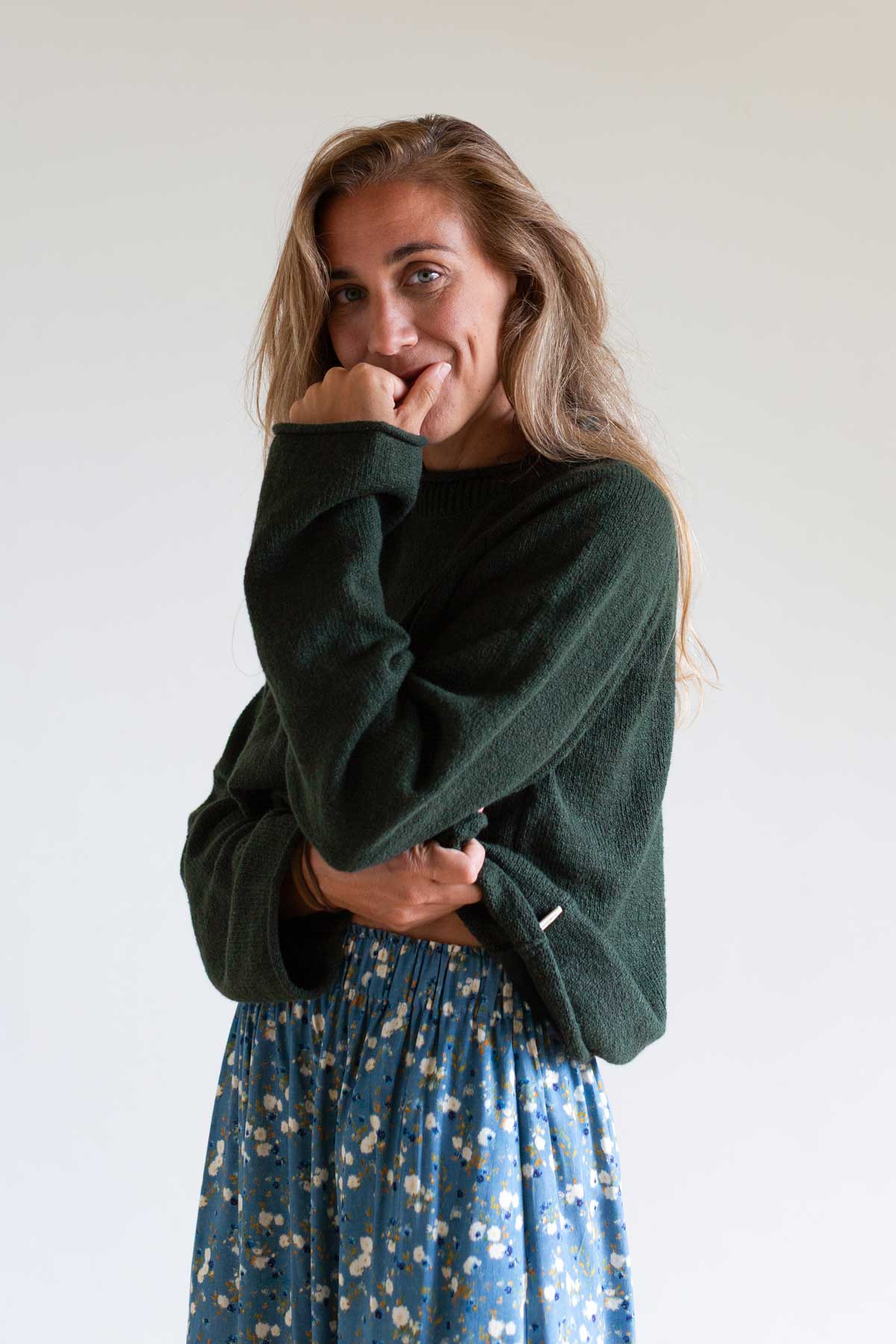 Woman wearing a dark green raglan knit sweater and a blue floral skirt.