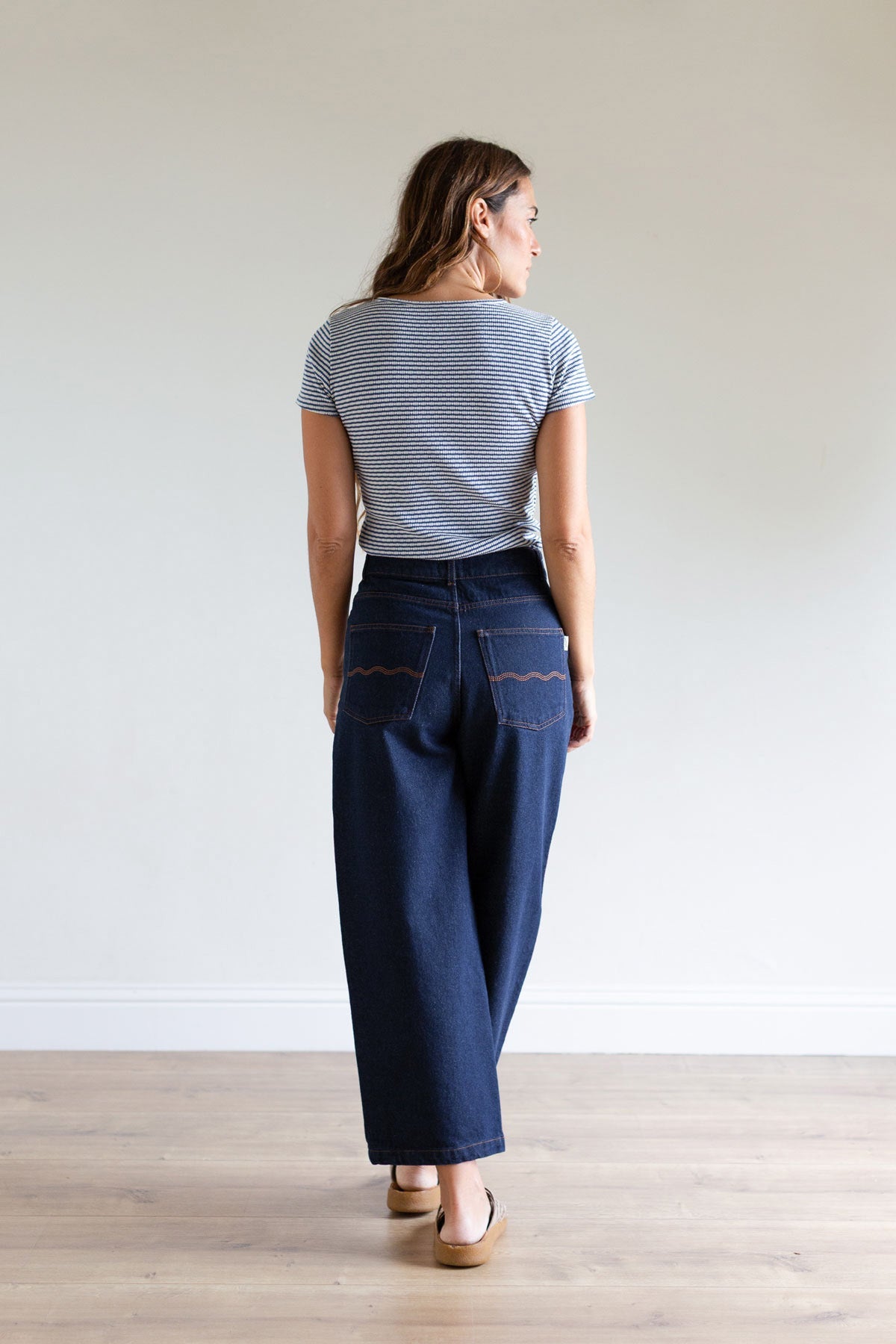 Full body back view of a woman wearing ankle-length wide-leg blue denim pants.