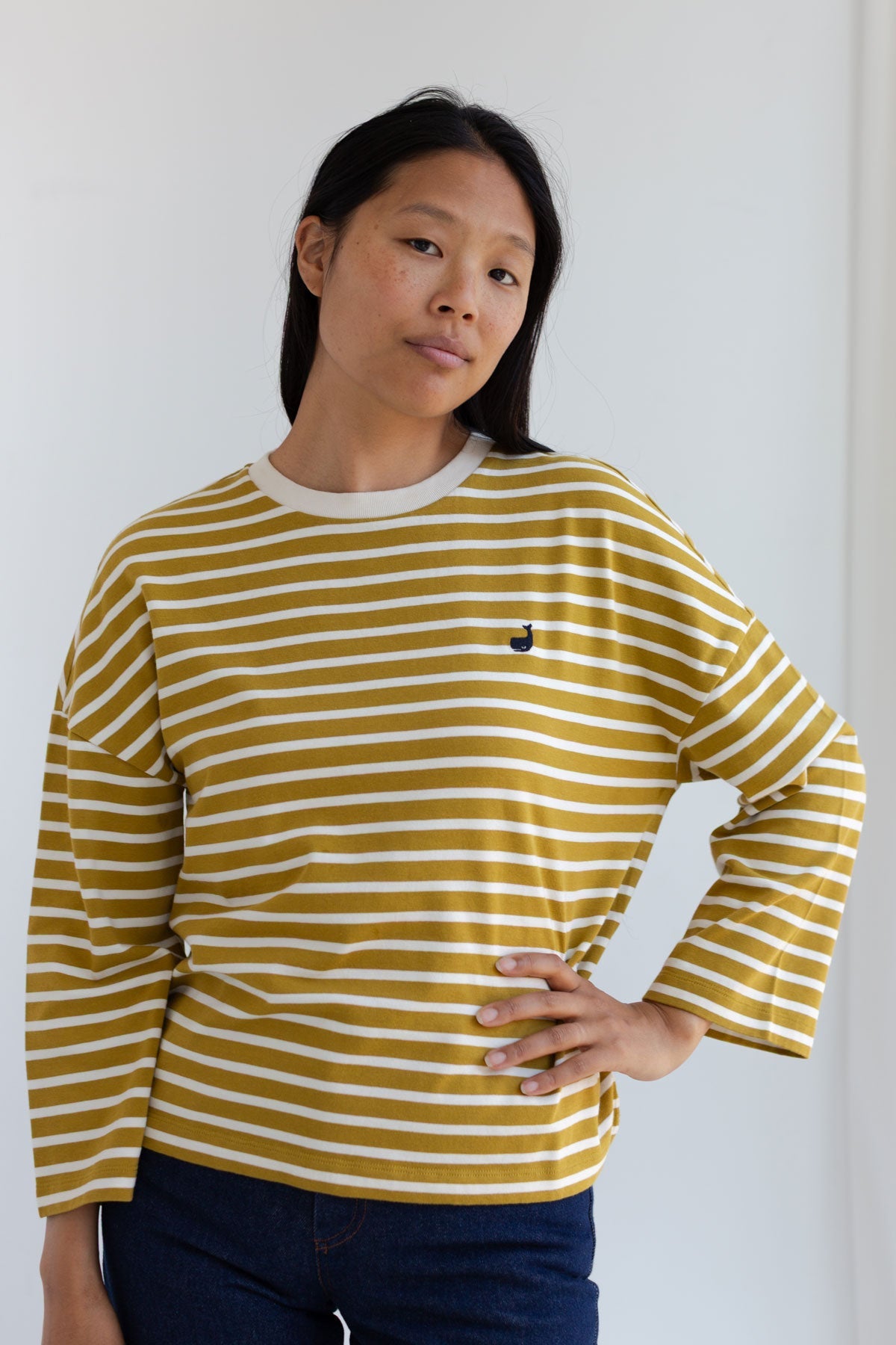 Woman with a hand on her hip wearing a mustard yellow striped long sleeve top.