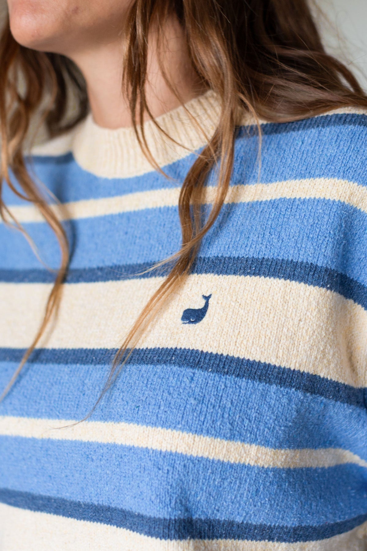 Close-up of a blue and cream striped sweater showing the embroidered whale logo.