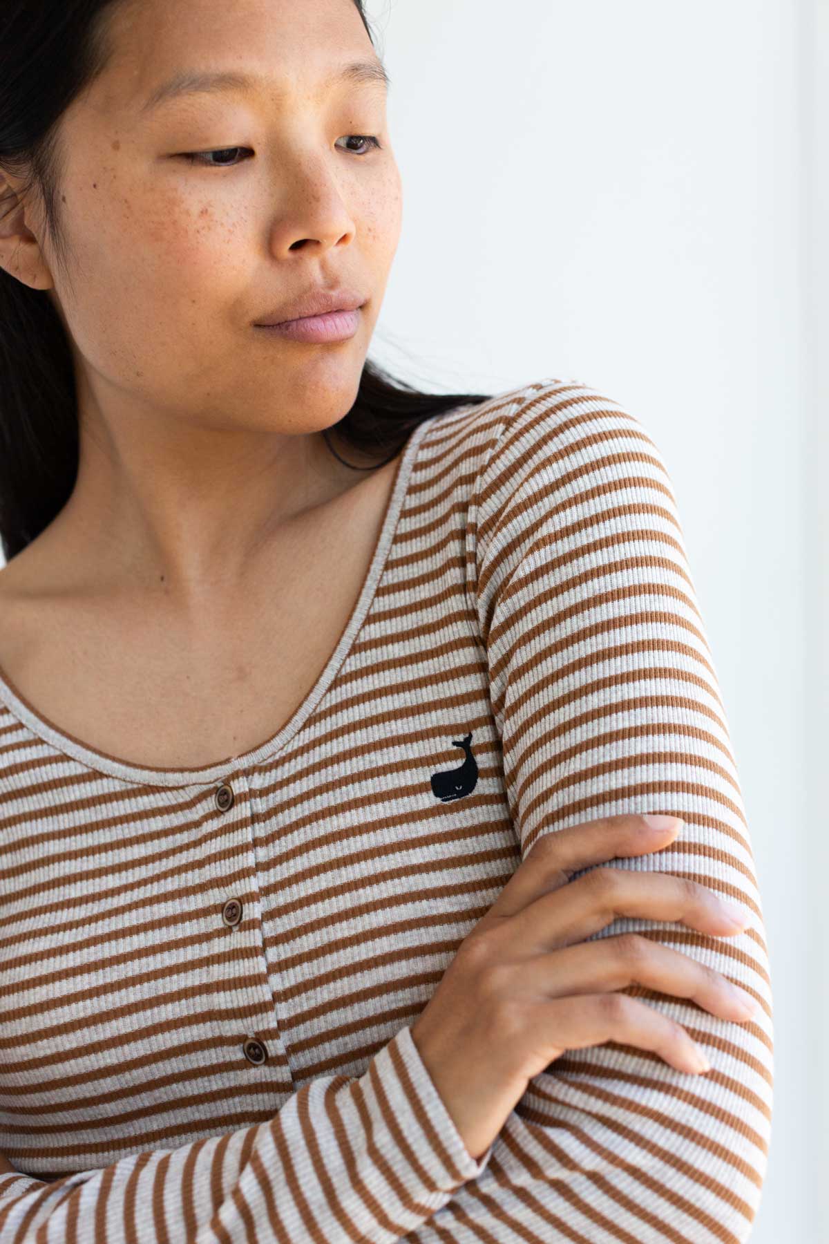 Close-up front view of a caramel striped top showing the embroidered whale logo.