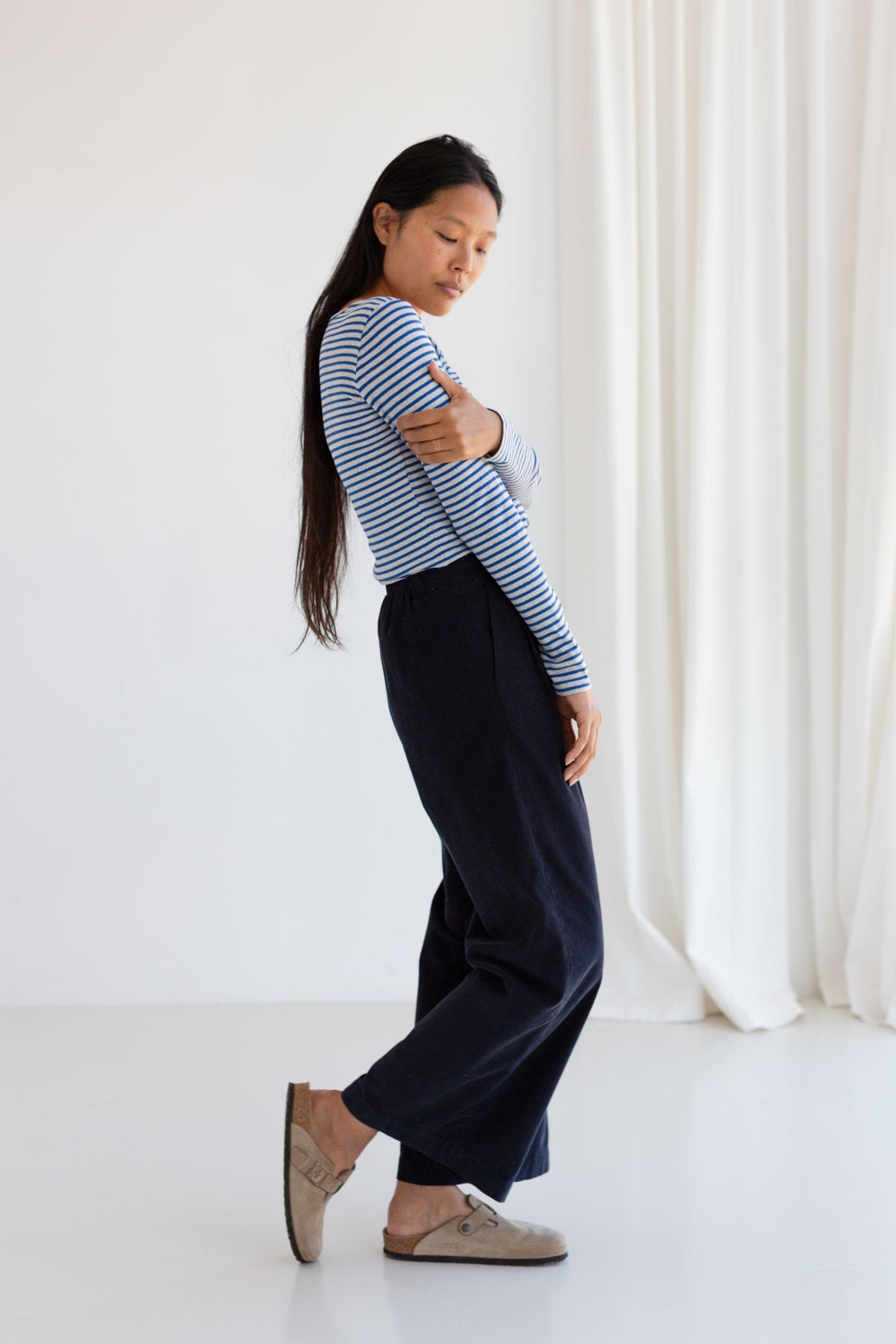 Side profile view of a woman with arms crossed in a blue striped ribbed top.