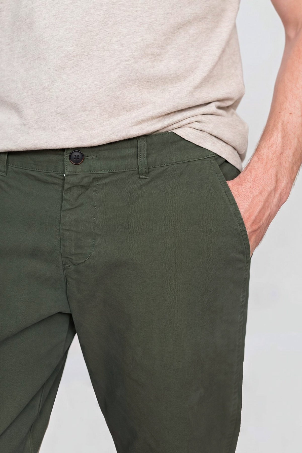 Close-up front view of the waistband, button closure, and side pocket on dark moss pants.